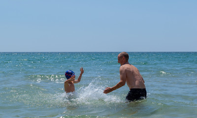 Father and son play in the water at sea. They splash water and laugh merrily. Sea water spray.