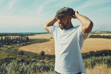 Portrait of confused male farmer looking into the camera and scratching his head. Close up of young doubtful man standing in the meadow on sunny day. Yellow field under blue sky at background.