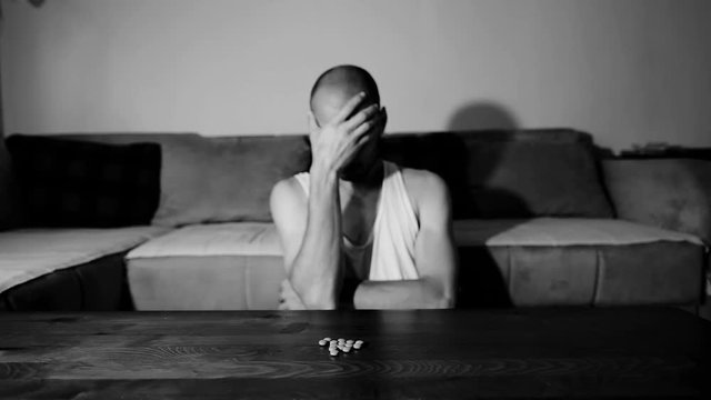 Depressed man suffering from suicidal depression want to commit suicide by overdose taking strong medicament drugs and pills pain killers sitting in his dark room selective focus moody dramatic look