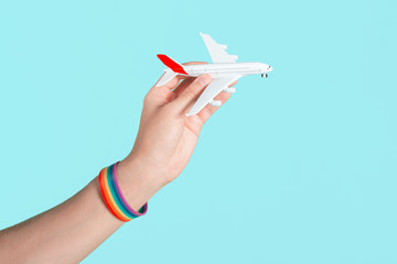 Hand with LGBT bracelet holding a toy plane. The concept of travel and air transport for gays and lesbians