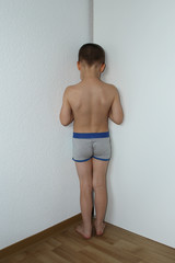 boy, junior schoolboy, standing in the corner undressed, facing the wall, punished by his parents...