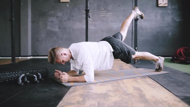 High performance triathlon or marathon exercises. Man in good fit does plank alternating leg lifts for improving sports training. Available exercises for office workers. Intermediate no equipment