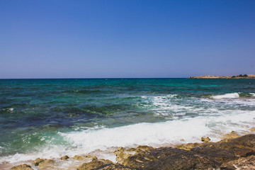 Fototapeta na wymiar Beautiful view of the clear Mediterranean sea with white foam wave on the rocky shore. Sunny seascape in Cyprus