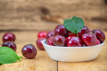Fresh cherries in the white bowl on wood table