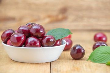 Fresh cherries in the white bowl on wood table