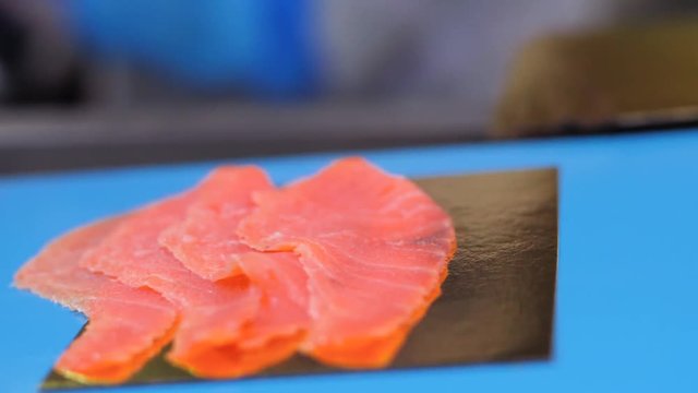 Premium Sliced Smoked Salmon moving on a conveyor belt, slow motion, close up.