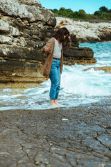woman walking by rocky sea beach at sunny windy day. summer vacation