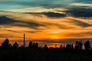 Dark dramatic colorful sky with clouds after sunset. Black horizon with trees and a chimney. Summer evening landscape.