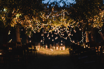 Coziness and style. Modern event design. Lounge zone and european traditional wedding ceremony decoration outdoors in the evening, decorated with candles and lights.