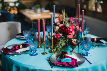 Coziness and style. Modern event design. Table setting at wedding reception. Floral compositions with beautiful flowers and greenery, candles, laying and plates on decorated table.