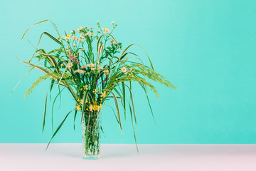 Obraz premium summer bouquet of green herbs and chamomile flowers in a glass vase on a pastel mint background with copy space