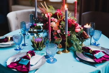 Coziness and style. Modern event design. Table setting at wedding reception. Floral compositions with beautiful flowers and greenery, candles, laying and plates on decorated table.