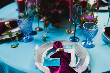 Coziness and style. Modern event design. Table setting at wedding reception. Floral compositions with beautiful flowers and greenery, candles, laying and plates on decorated table.