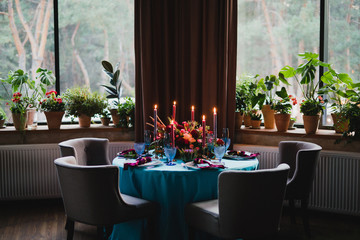 Coziness and style. Modern event design. Table setting at wedding reception. Floral compositions with beautiful flowers and greenery, candles, laying and plates on decorated table.