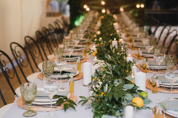 Coziness and style. Modern event design. Table setting at wedding reception. Floral compositions with beautiful flowers and greenery, candles, laying and plates on decorated table.
