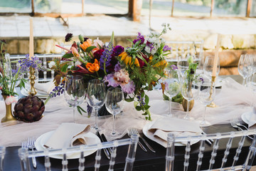 Coziness and style. Modern event design. Table setting at wedding reception. Floral compositions with beautiful flowers and greenery, candles, laying and plates on decorated table.