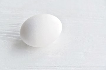 White chicken egg with selective focus on blurred textured gray background. Fresh organic fragility egg on neutral backdrop, soft focus. Ingredient for healthy diet breakfast. Easter symbol 