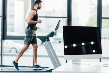 Fototapeta premium selective focus of computer with blank screen near sportsman running on treadmill at sports center