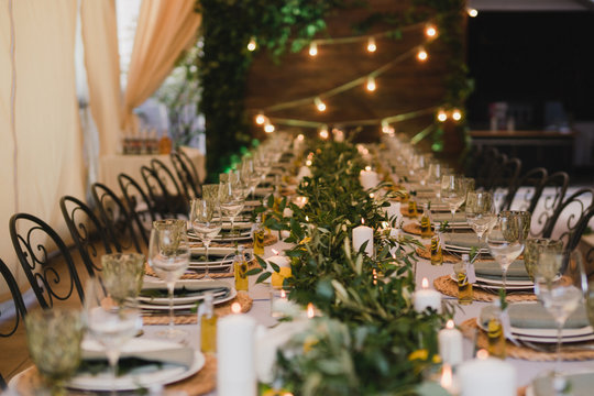 Coziness and style. Modern event design. Table setting at wedding reception. Floral compositions with beautiful flowers and greenery, candles, laying and plates on decorated table.