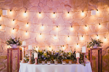 Coziness and style. Modern event design. Table setting at wedding reception. Floral compositions with beautiful flowers and greenery, candles, laying and plates on decorated table.