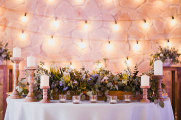 Coziness and style. Modern event design. Table setting at wedding reception. Floral compositions with beautiful flowers and greenery, candles, laying and plates on decorated table.
