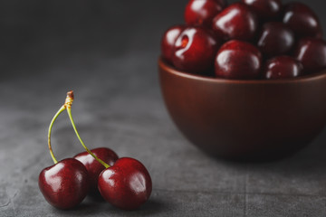 Ripe and juicy cherry berries on a black textural background in a brown cup, with water drops. Top view, close-up, Macro.