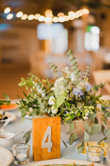 Coziness and style. Modern event design. Table setting at wedding reception. Floral compositions with beautiful flowers and greenery, candles, laying and plates on decorated table.
