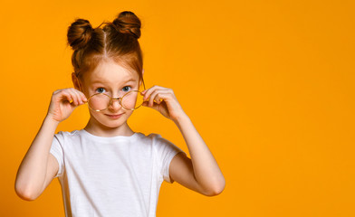 Beautiful young girl with red hair with a bagel in her stylish glasses looks at you in the frame.