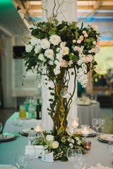 Coziness and style. Modern event design. Table setting at wedding reception. Floral compositions with beautiful flowers and greenery, candles, laying and plates on decorated table.