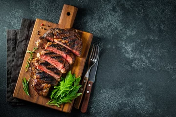 Fototapeten Sliced steak ribeye, grilled with pepper, garlic, salt and thyme served on a wooden cutting Board on a dark stone background. Top view with copy space. Flat lay © Vasiliy