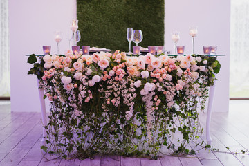 Coziness and style. Modern event design. Table setting at wedding reception. Floral compositions with beautiful flowers and greenery, candles, laying and plates on decorated table.