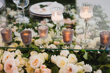 Coziness and style. Modern event design. Table setting at wedding reception. Floral compositions with beautiful flowers and greenery, candles, laying and plates on decorated table.