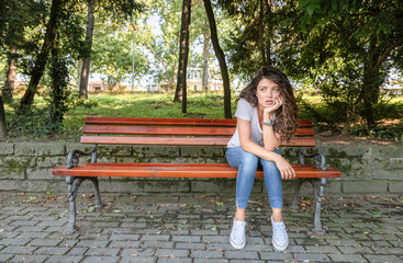 Young girl or woman sitting alone on the park bench feeling depressed and sad after she had argue and fight with her boyfriend or husband and she thinking about her life with sadness on her face
