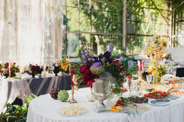 Coziness and style. Modern event design. Table setting at wedding reception. Floral compositions with beautiful flowers and greenery, candles, laying and plates on decorated table.