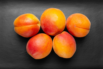 Ruddy apricots on a dark background. Top view fresh juicy apricots stacked on a dark clay plate.