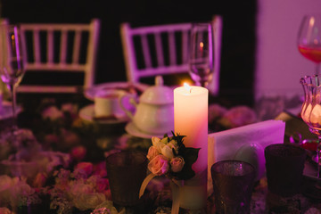 Coziness and style. Modern event design. Table setting at wedding reception. Floral compositions with beautiful flowers and greenery, candles, laying and plates on decorated table.