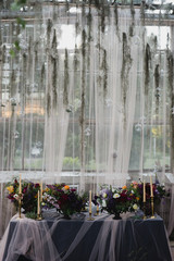 Coziness and style. Modern event design. Table setting at wedding reception. Floral compositions with beautiful flowers and greenery, candles, laying and plates on decorated table.