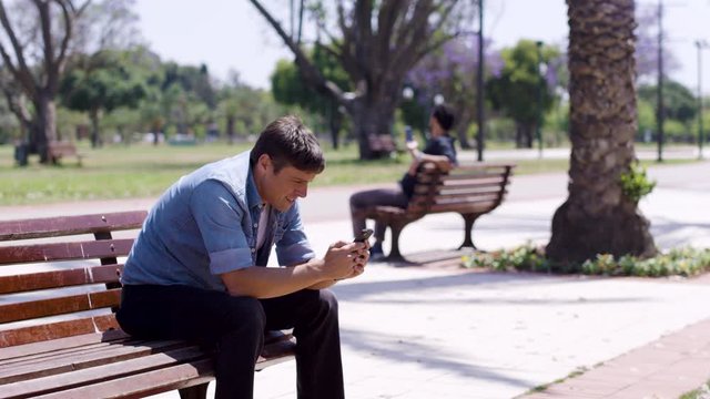 Frustration from technology. A man smashes his phone on a bench and throws it.