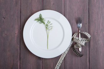 Dieting concept - white plate with dill, fork and centimeter tape
