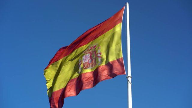 big spanish flag fluttering in blue sky