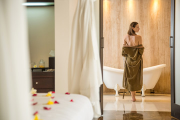 Young woman in the bathroom wearing a robe getting ready to take a bath in the tub, wellbeing body care and beauty concept, spa weekend