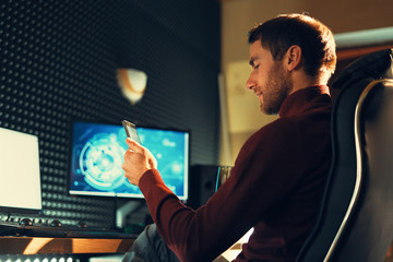 Young man working in the studio using a smartphone and computer.