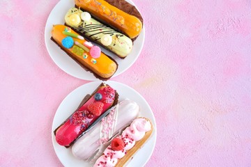 Set of colorful traditional French eclair dessert with creative decor on pink textured background, selective focus. Delicious profiterole stuffed with gluten free cream decorated with fresh berries