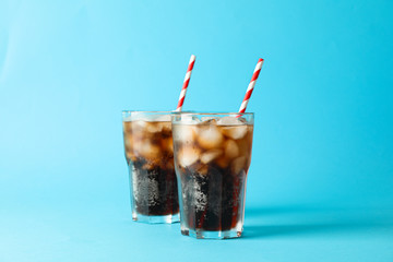 Glasses with cold cola and tubule on blue background, space for text