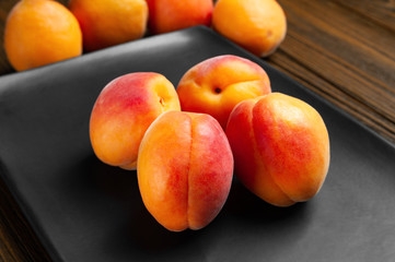 Naklejka na ściany i meble Apricots on a dark background. Fresh juicy ruddy apricots are stacked on a dark clay plate.