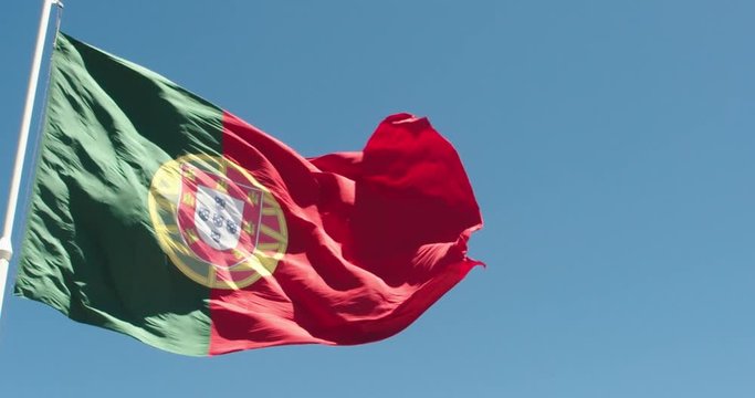 Flag Of Portugal waving on the wind, on the sunny day against bright blue sky, slow motion close up shot