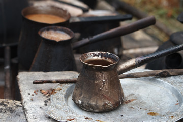 Boiling coffee in turkish cezva on a grate over a burning bonfire, a camping concept