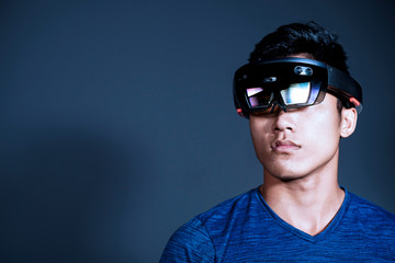 The Asian young man with glasses of virtual reality. Experience VR hololens headset in studio with advanced technology.