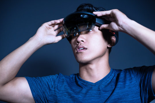 The Asian young man with glasses of virtual reality. Experience VR hololens headset in studio with advanced technology. Surprise face testing new device.