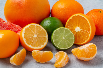 group of whole and sliced citrus fruits - tangerines, lemons, limes, oranges, grapefruits on the surface of the gray table - image